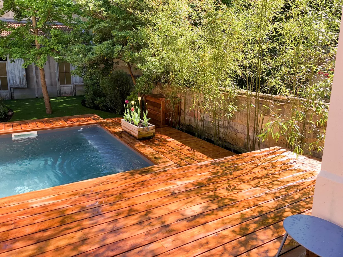 Jardin d'échoppe aménagé avec une terrasse en bois, une piscine et diverses plantations 