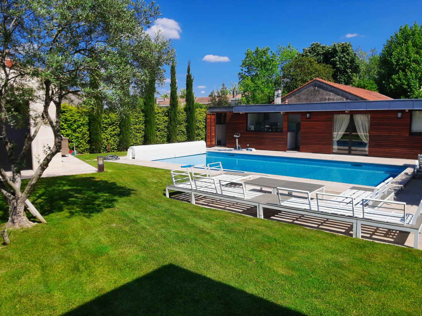 Aménagement d'un jardin atypique dans un ancien hangar, comprenant une piscine, des zones de plantations, une terrasse en bois et un espace engazonné