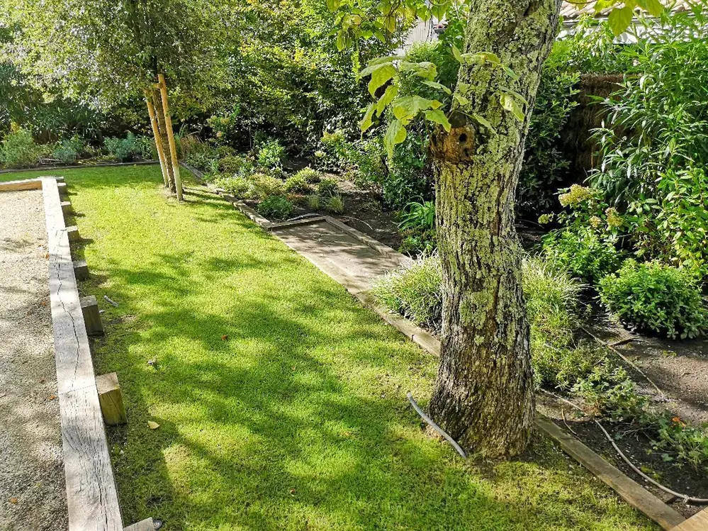 Aménagement de jardin avec espace pétanque, une terrasse bois et diverses plantations